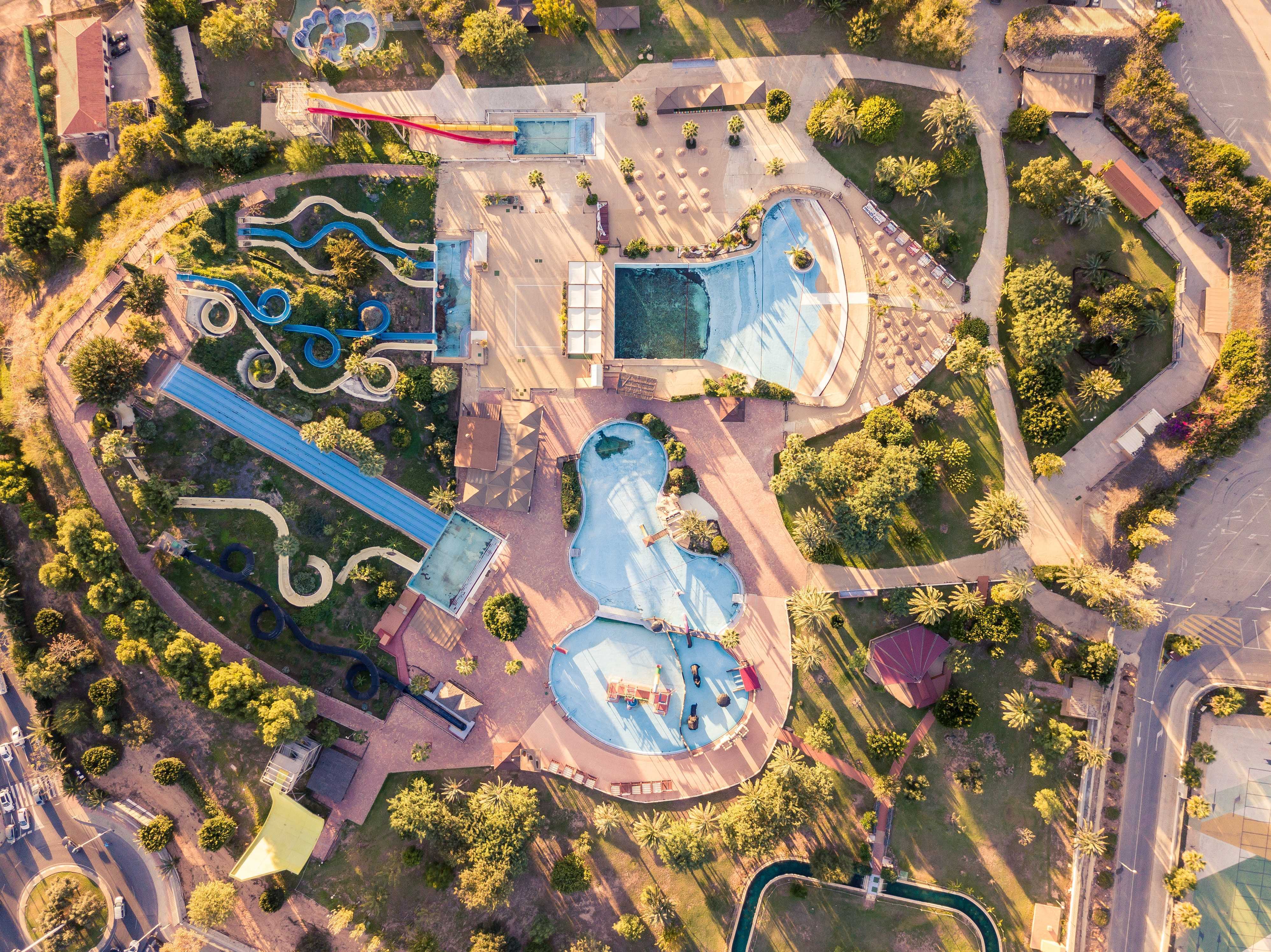 Aerial view of a resort-style water park with pools, winding blue water slides, sun loungers, and landscaped gardens